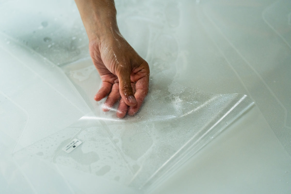 Hand peeling clear paint protection film from backing paper during WildWrap DIY PPF installation