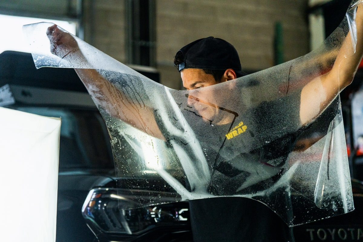 Wet clear PPF being transferred from backing paper to a vehicle during WildWrap DIY installation