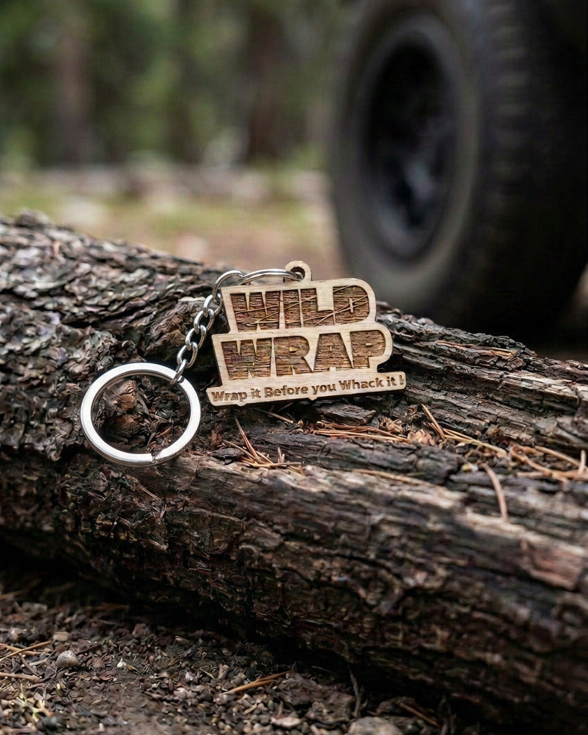 Wild Wrap mahogany logo keychain resting on a log along a forest trail