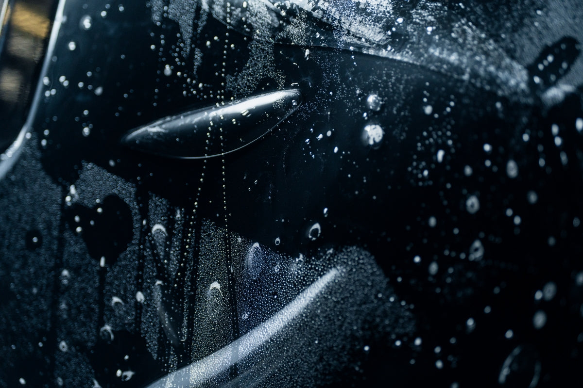 closup of ppf paint protection film with droplets and bubbles on black paint 